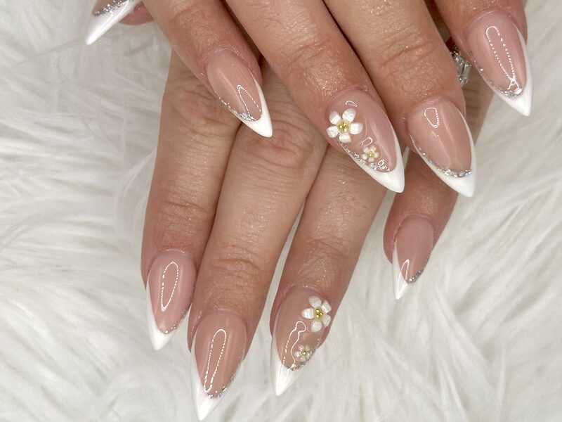 Long nude stiletto nails with white tips, 3D flowers, and rhinestones