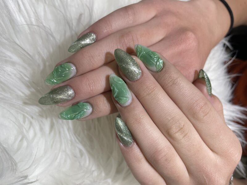 Emerald green stiletto nails with metallic leaf accents